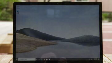 La Surface Laptop 4 de 15 pulgadas abierta sobre una mesa de picnic con un edificio de apartamentos rosa al fondo.  La pantalla muestra dunas de arena con un cielo azul.