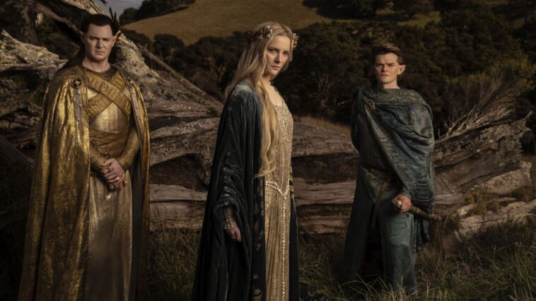 Galadriel, Gil-galad, and Elrond wear regal clothes as they stand in a field for a press photo for The Rings of Power