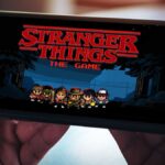 An image of a person holding a mobile phone in landscape mode with the Stranger Things: The Game title screen loaded up