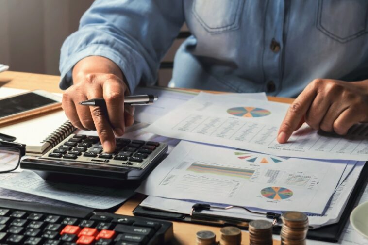 concepto de contabilidad.  mujer de negocios que trabaja usando calculadora con pila de dinero en la oficina