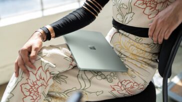 Un usuario sentado con un traje floral sostiene una Surface Laptop 5 cerrada en su regazo con el logotipo de Microsoft visible.