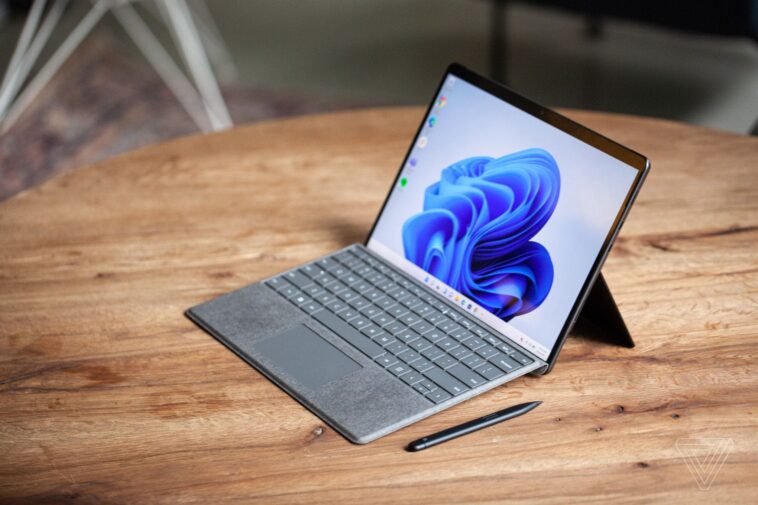 El Surface Pro 8 visto desde arriba y a la derecha sobre una mesa con el Surface Slim Pen 2 al lado y el Signature Keyboard adjunto.  La pantalla muestra un remolino azul sobre un fondo blanco.
