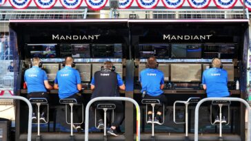 Los miembros del equipo Alpine leen pantallas de datos en vivo mientras están sentados en el área de boxes.