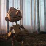 Pinocchio smiles as he crosses his arms in a forest in Guillermo del Toro