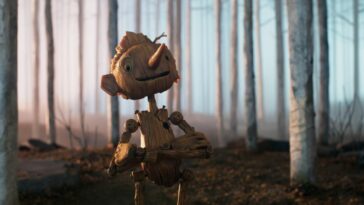 Pinocchio smiles as he crosses his arms in a forest in Guillermo del Toro