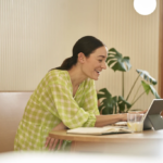 Mujer sentada en la cocina trabajando en modo portátil tabletin 2 en 1.