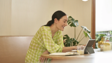 Mujer sentada en la cocina trabajando en modo portátil tabletin 2 en 1.