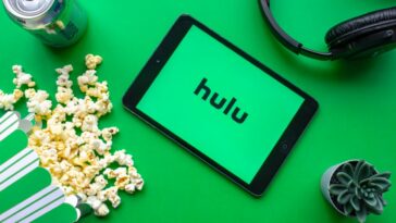 An iPad with the Hulu logo on the screen on a green background with popcorn and headphones