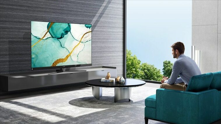 A man watching a Hisense TV in a modern looking living room.