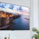 The LG G3 OLED mounted on a white wall displaying a scene from a coastal town