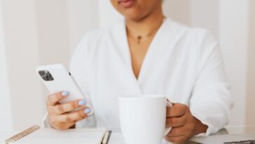 Esta foto muestra a alguien mirando un teléfono móvil y tomando café.