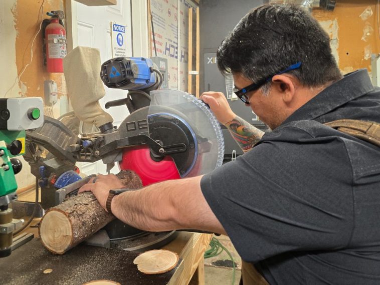 Jimmy, con equipo de protección, está trabajando en un taller de carpintería y cortando un tronco de madera.