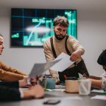 Un equipo colaborativo trabajando durante una reunión, analizando datos financieros. La gente discute activamente gráficos, muestra un espacio de trabajo profesional e ideas innovadoras.